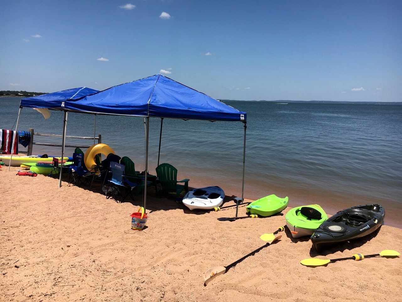 Une plage avec des parasols bleus, des kayaks, des planches de paddle et des chaises de plage.