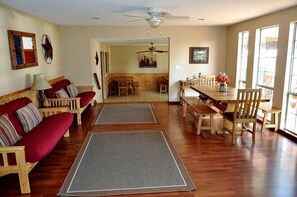 A spacious living room with a wooden floor, a red sofa, a dining table with chairs, and a ceiling fan. - Spacious Lakefront Home with Beach Access and Sports Courts for Fun-Filled stays in Buchanan Dam, Texas (Buchanan Dam)