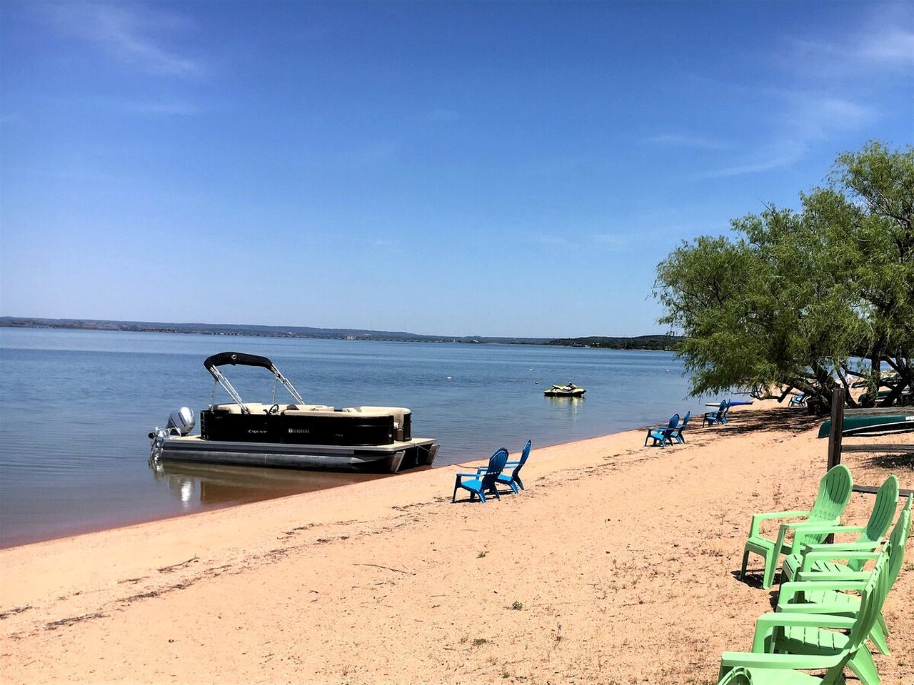 A beach with a boat docked, chairs, and a clear sky.