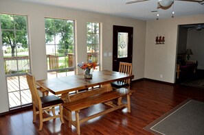 A dining room with a wooden table and chairs, a vase of flowers, and large windows with a view of a deck and trees. - Spacious Lakefront Home with Beach Access and Sports Courts for Fun-Filled stays in Buchanan Dam, Texas (Buchanan Dam)
