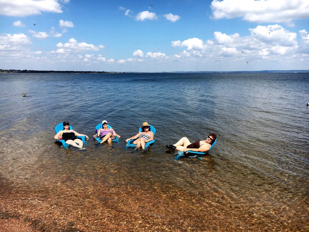 A group of people sitting on blue chairs in shallow water.