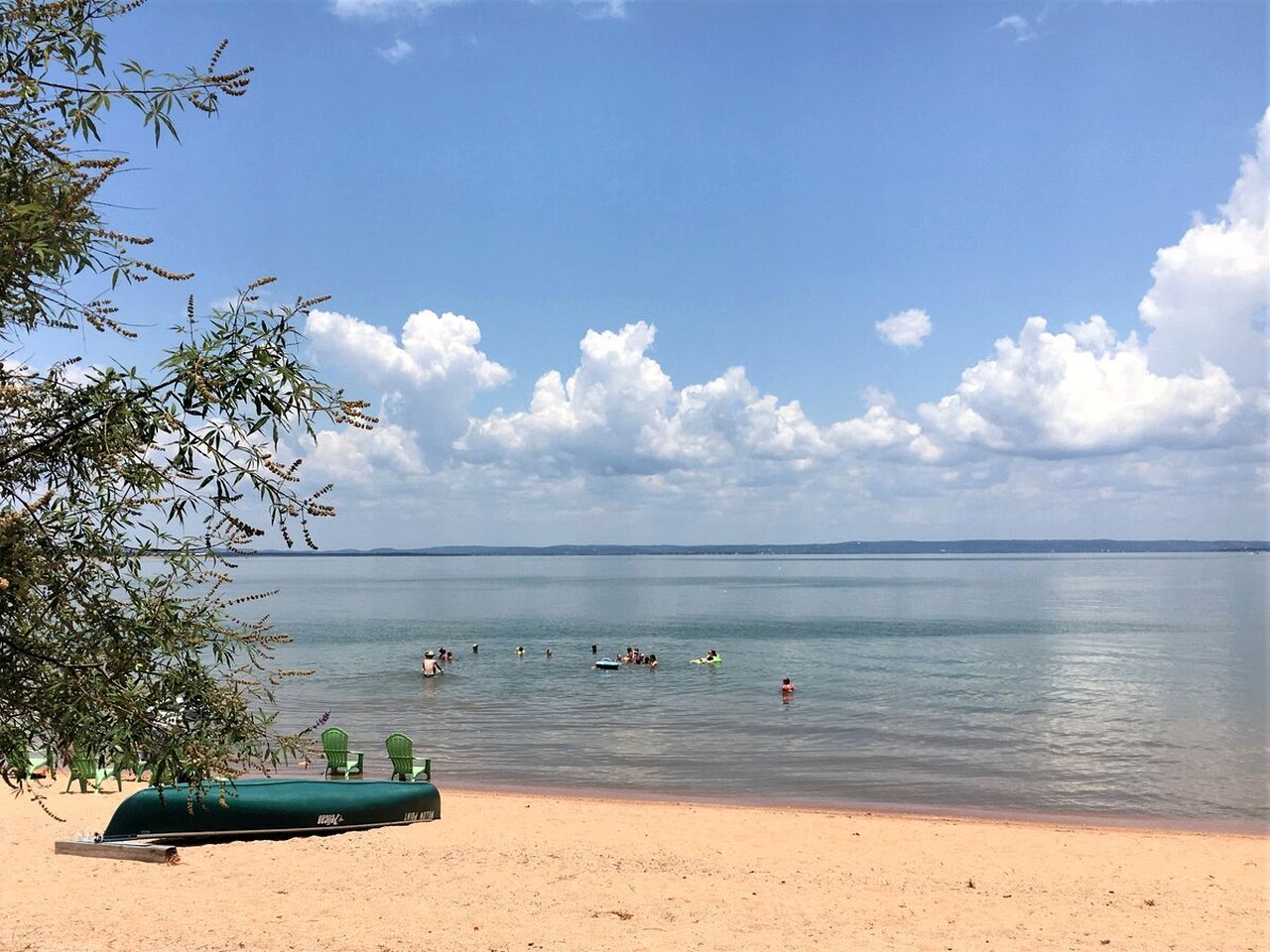 Une plage avec une mer calme, quelques personnes qui se baignent et un bateau vert sur le sable.