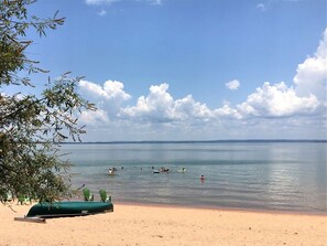 A beach with a calm sea, a few people swimming, and a green boat on the sand. - Spacious Lakefront Home with Beach Access and Sports Courts for Fun-Filled stays in Buchanan Dam, Texas (Buchanan Dam)