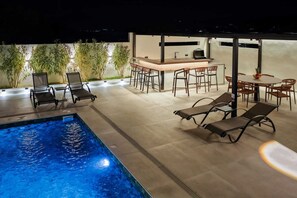 A pool area with lounge chairs, a bar, and a dining table. - Ria Oasis Residence, Luxury 3-Bedroom Apartment with Private Pool (Agios Nikolaos)
