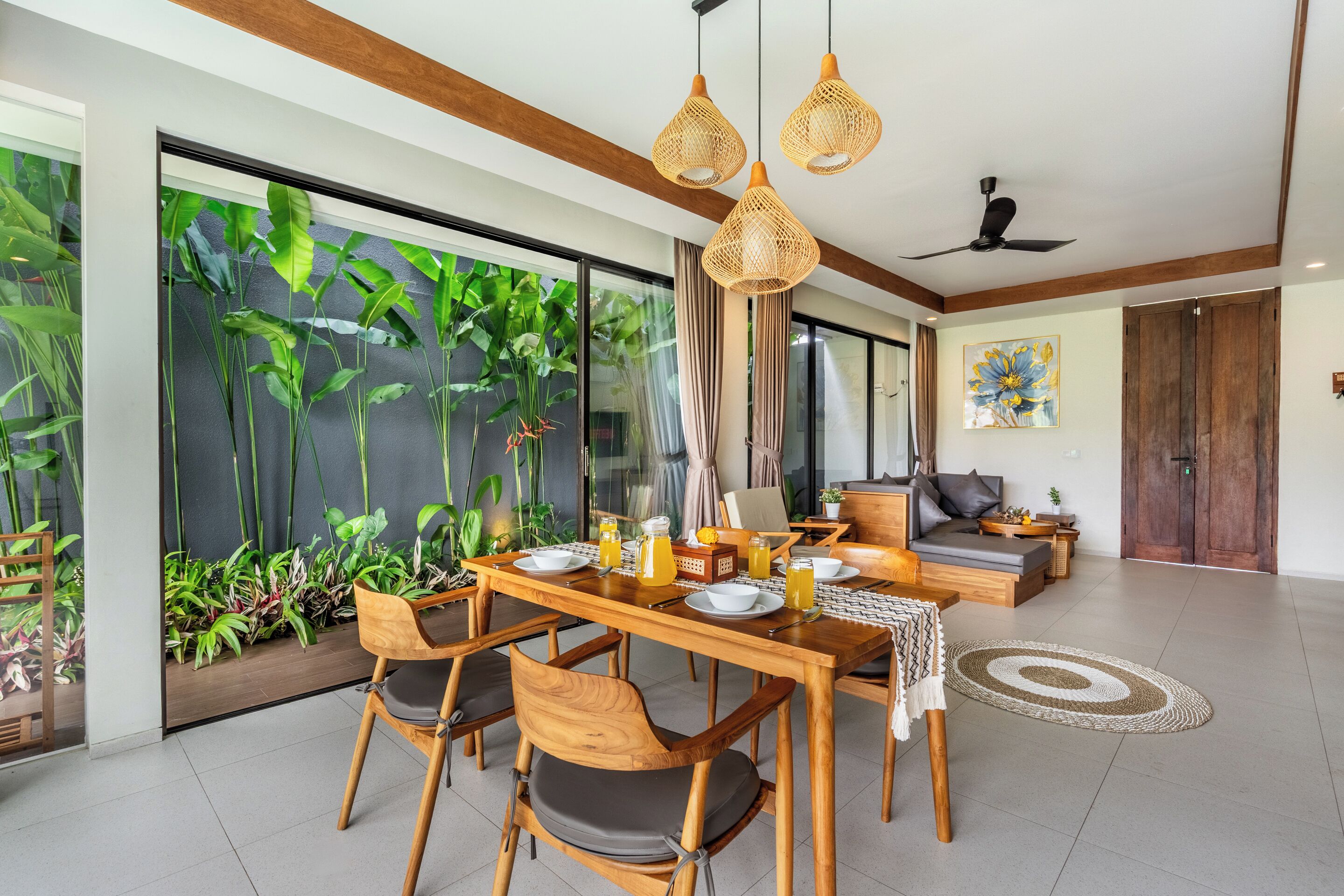 Un comedor con una mesa de madera, sillas y un ventanal con plantas.
