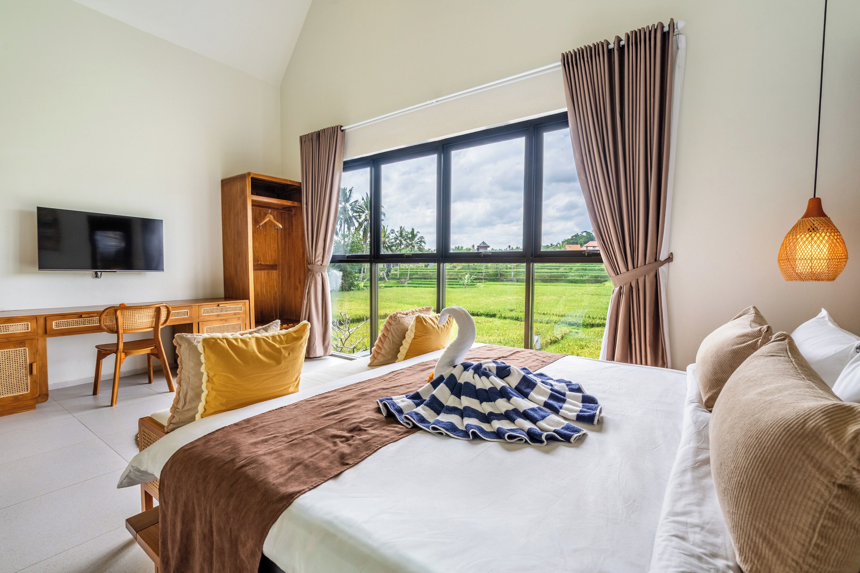 Een slaapkamer met een groot bed, een bureau, een stoel, een televisie en uitzicht op een groen landschap.