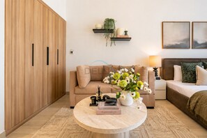 Ein modernes Wohnzimmer mit einer Couch, einem Couchtisch mit Büchern, einer Pflanze und einem Bett mit Kissen.