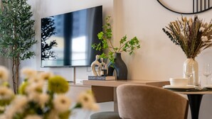 Ein modernes Wohnzimmer mit Fernseher, einem Esstisch mit Geschirr und Gläsern sowie dekorativen Pflanzen.