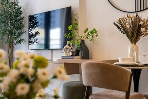 Ein modernes Wohnzimmer mit Fernseher, einem Esstisch mit Geschirr und Gläsern sowie dekorativen Pflanzen.