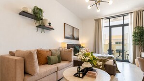 Ein modernes Wohnzimmer mit einem beigefarbenen Sofa, einem runden Couchtisch und einem großen Fenster mit Vorhängen.