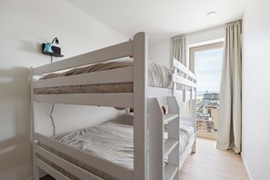 A bunk bed room with a city view, a small shelf with a lamp, and a window with curtains. - 2 bedroom accommodation in OOSTENDE (OOSTENDE)