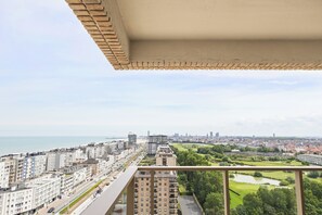 Un edificio alto con varios balcones, vista a un paisaje urbano y una masa de agua al fondo.