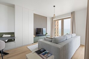 A modern living room with a grey sofa, a flat-screen TV, a dining table, and a view of the sea through large windows. - 2 bedroom accommodation in OOSTENDE (OOSTENDE)