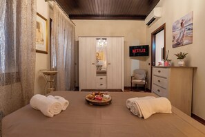 A hotel room with a bed, a minibar, a TV, and a painting on the wall. - Il Vicolo Di Ortigia | Authentic Sicilian Home in the Historic City Center (Siracusa)