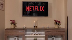 Habitació amb un armari de fusta, un televisor fixat a la paret i dos vasets amb flors.