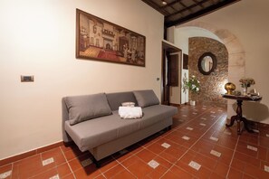A room with a grey sofa, a painting, a stone archway, and a tiled floor. - Il Vicolo Di Ortigia | Authentic Sicilian Home in the Historic City Center (Siracusa)