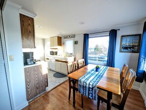 A compact kitchen with a dining area, a sign reading 'HAPPY PLACE', and a view through the window. - Cozy Waterfront Cottage with Private Beach and Fire Pit Near Gouldsboro, Maine (Gouldsboro)