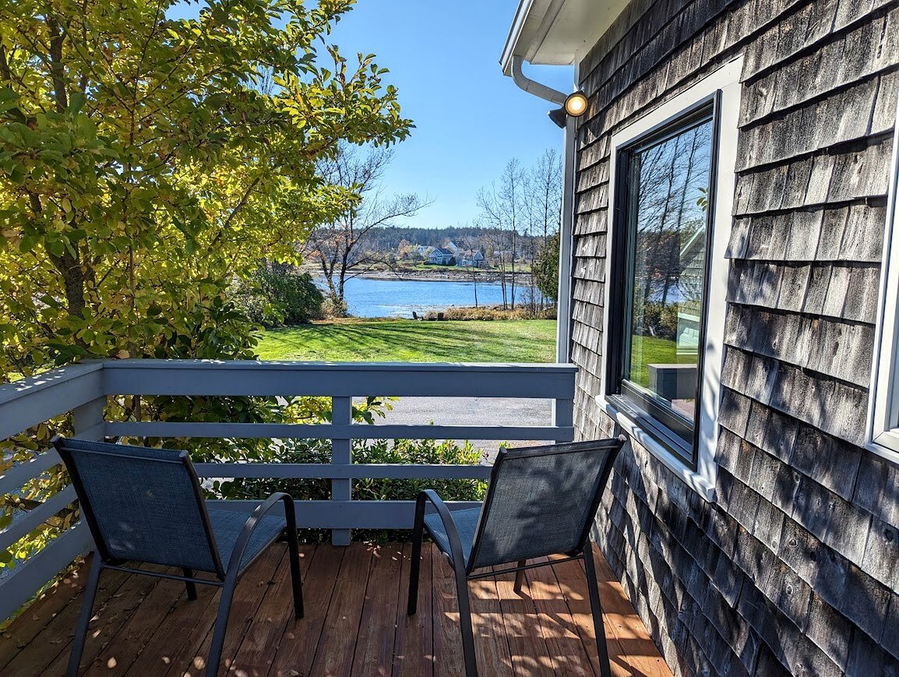 A deck with two chairs overlooking a lake and a house with a window.