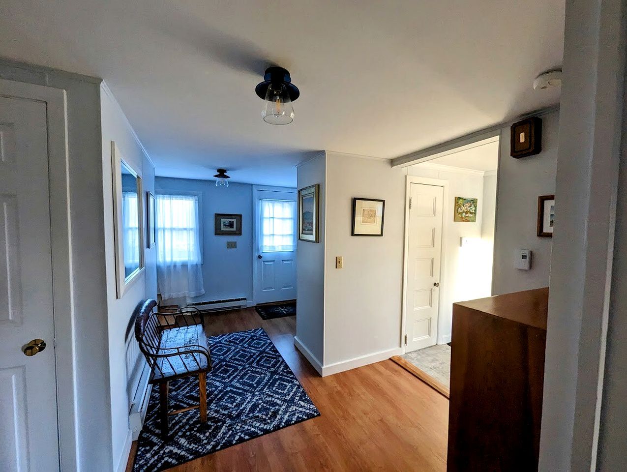 A hallway with a wooden floor, a patterned rug, a metal bench, and a ceiling fan.