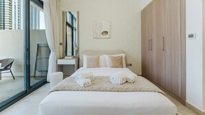 A hotel room with a bed, a large wardrobe, a bathroom with a sink, and a view of high-rise buildings. - PVH - Azizi Riviera 37 Vibrant Studio (Dubai)
