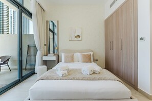 A hotel room with a bed, a large wardrobe, a bathroom with a sink, and a view of high-rise buildings. - PVH - Azizi Riviera 37 Vibrant Studio (Dubai)