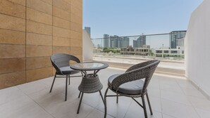 A balcony with two wicker chairs and a small table, overlooking a cityscape with high-rise buildings. - PVH - Azizi Riviera 37 Vibrant Studio (Dubai)