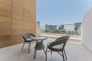 A balcony with two wicker chairs and a small table, overlooking a cityscape with high-rise buildings. - PVH - Azizi Riviera 37 Vibrant Studio (Dubai)