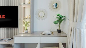 A modern hotel room with a flat-screen TV, a desk with a plant, decorative wall mirrors, and a neatly arranged dining set. - PVH - Azizi Riviera 37 Vibrant Studio (Dubai)