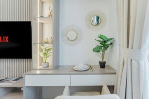 A modern hotel room with a flat-screen TV, a desk with a plant, decorative wall mirrors, and a neatly arranged dining set. - PVH - Azizi Riviera 37 Vibrant Studio (Dubai)