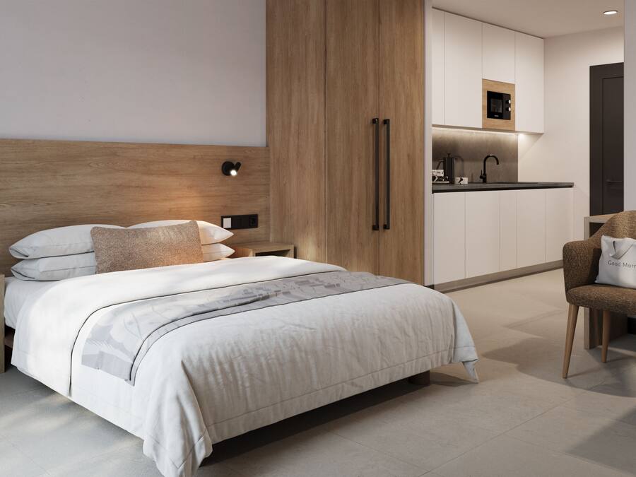 A modern bedroom with a large bed, bedside tables, a nightstand, a chair, and a kitchenette area.