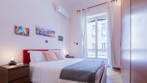 Ein Schlafzimmer mit Bett, Nachttischen, einem Fenster mit Vorhängen und Wandbildern.