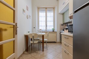 A compact kitchen with a dining table, chairs, a refrigerator, and a window with curtains. - Galliari Comfort Home by Wonderful Italy (Turin)