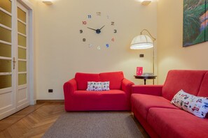 Ein Zimmer mit einem roten Sofa, einer Wanduhr, einer Lampe und einer Glastür.