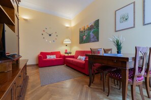 A living room with a red sofa, a wooden dining table, and a clock on the wall. - Galliari Comfort Home by Wonderful Italy (Turin)