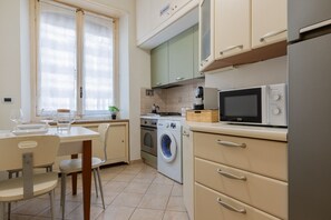A compact kitchen with a washing machine, microwave, and a dining area with chairs and a table. - Galliari Comfort Home by Wonderful Italy (Turin)