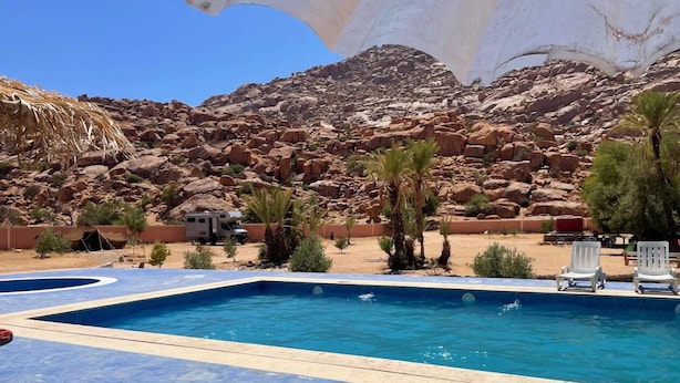 A swimming pool with a blue tiled deck, surrounded by palm trees and a rocky landscape. - Tagtout (TAFRAOUT)