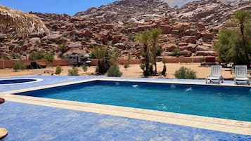 Une piscine dotée d’une terrasse carrelée de carreaux bleus, entourée de palmiers et bordée d’un paysage rocheux.
