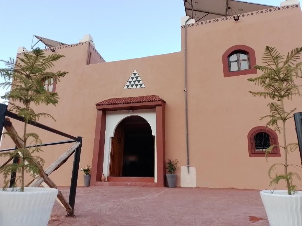 A building entrance with a red-tiled roof, a triangular window design, and potted plants.
