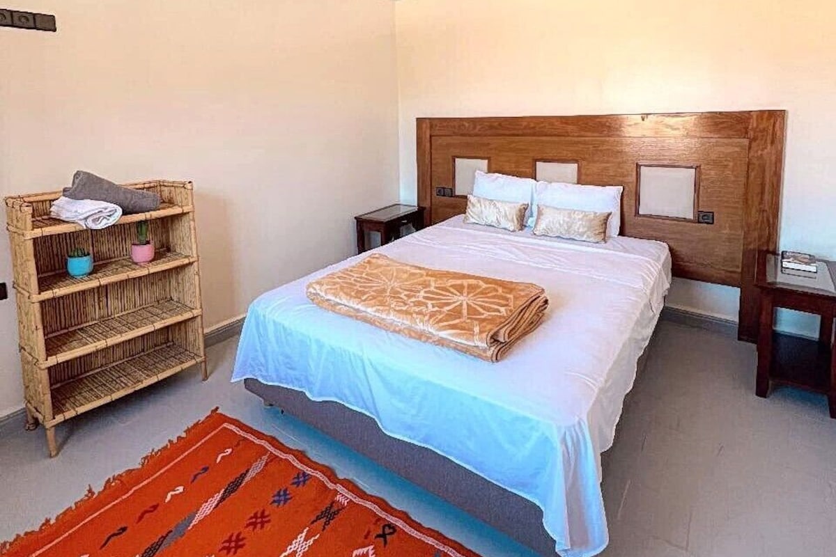 Ein Schlafzimmer mit einem großen Bett, einem Holzkopfstück, Nachttischen, einem gewebten Regal und einem gemusterten Teppich.