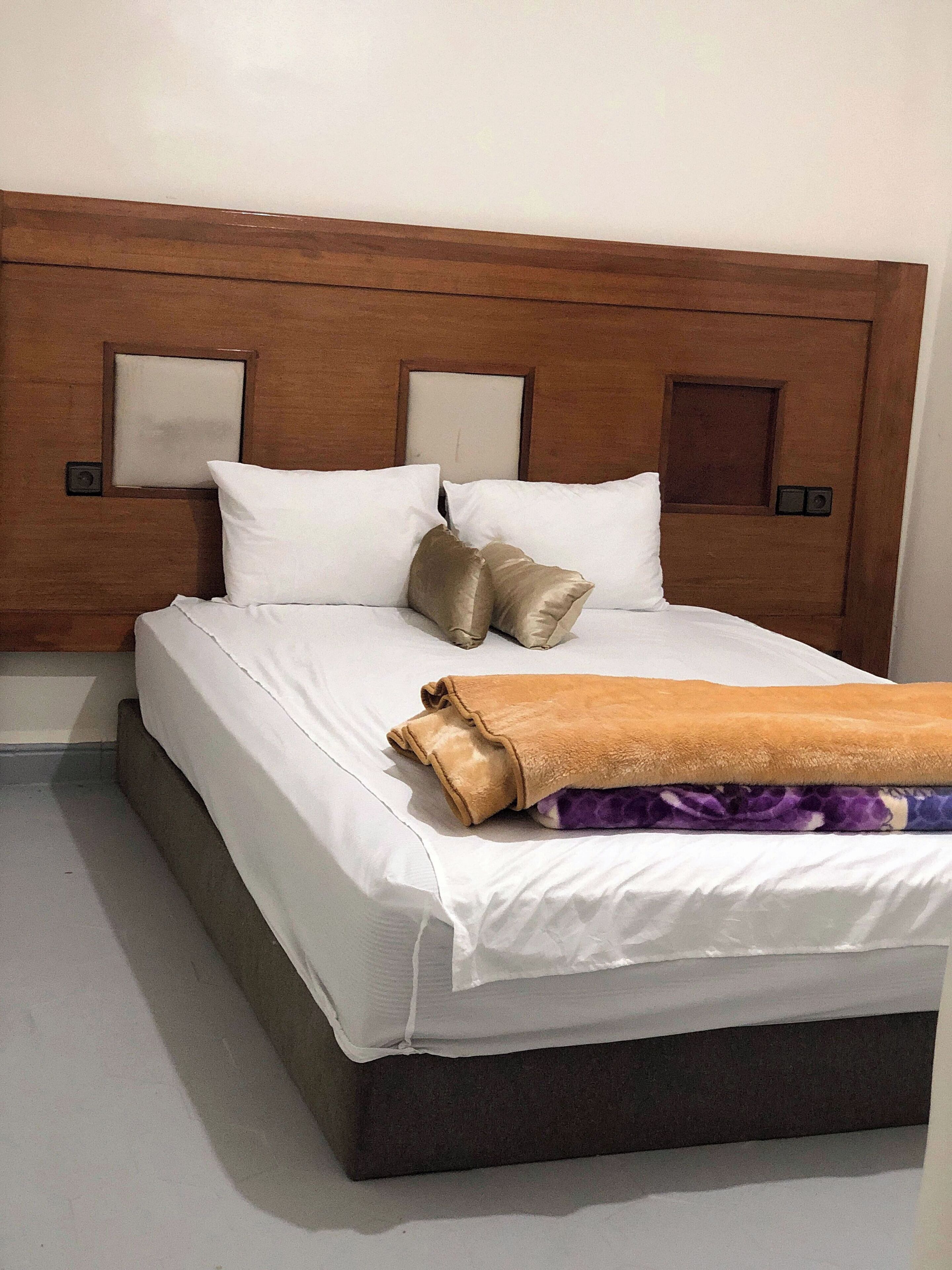A hotel room with a wooden headboard, white bedding, and a brown throw blanket.