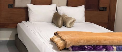 A hotel room with a wooden headboard, white bedding, and a brown throw blanket.
