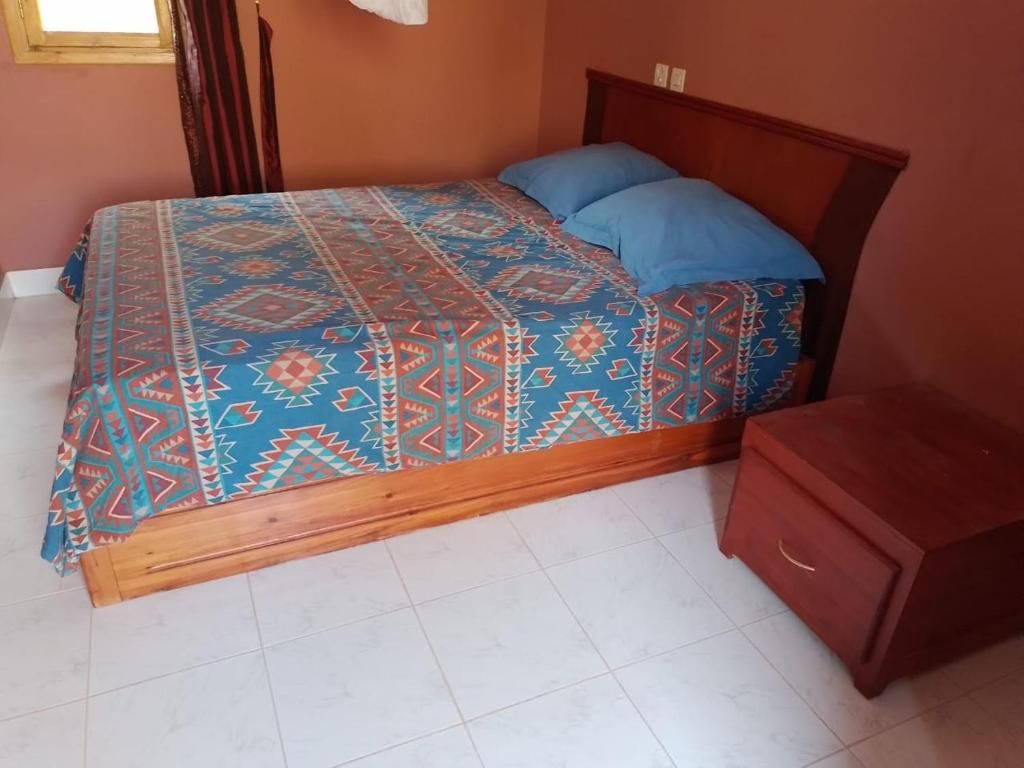 Un lit avec une couvre-lit à motifs et des oreillers bleus, une tête de lit en bois et une petite table de chevet en bois.
