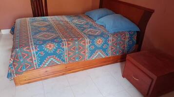 Un lit avec une couvre-lit à motifs et des oreillers bleus, une tête de lit en bois et une petite table de chevet en bois.