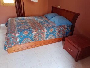 A bed with a patterned bedspread and blue pillows, a wooden headboard, and a small wooden nightstand.