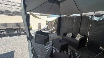 An outdoor patio with a table and chairs, a sofa, and a large umbrella providing shade.