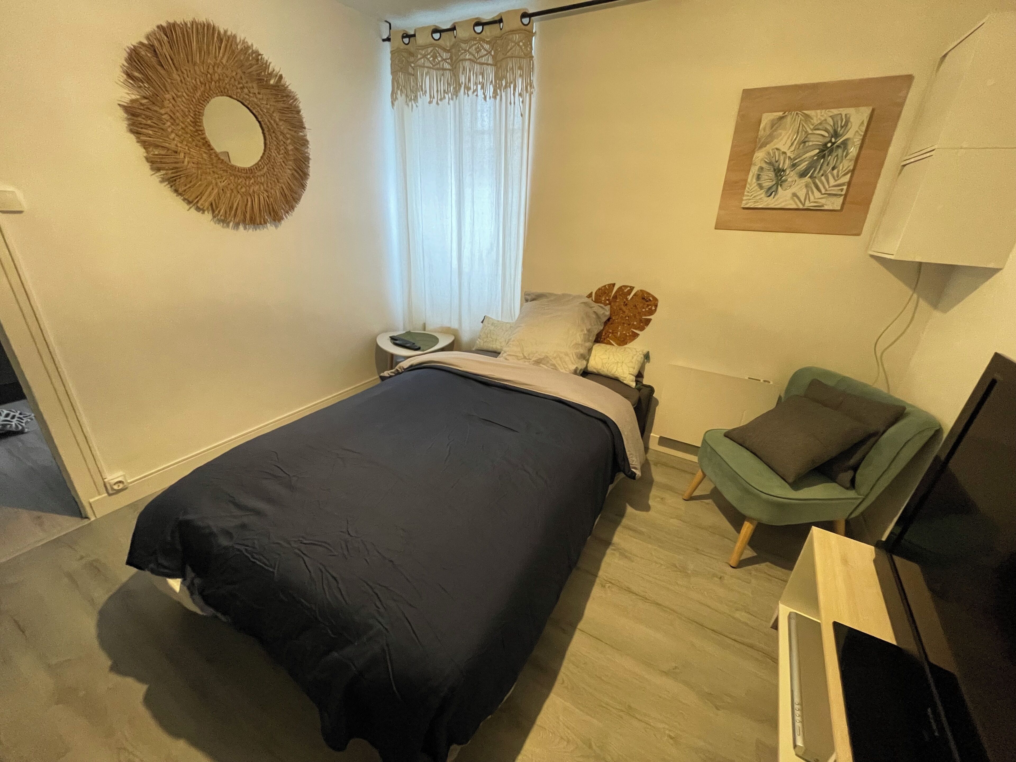 Un dormitorio con cama, mesita de noche, silla, televisión y un cuadro colgado en la pared.