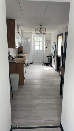 A hallway with a kitchen on the left, a dining area with a table and chairs, and a large window at the end.