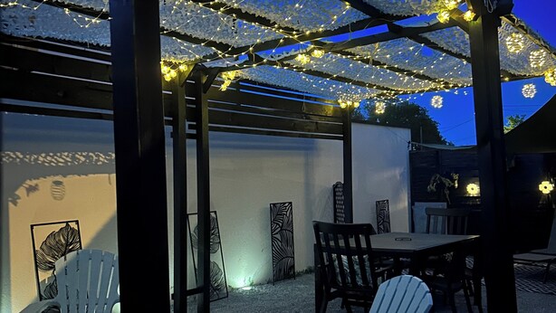 A covered outdoor seating area with chairs and tables, string lights, and decorative wall art.