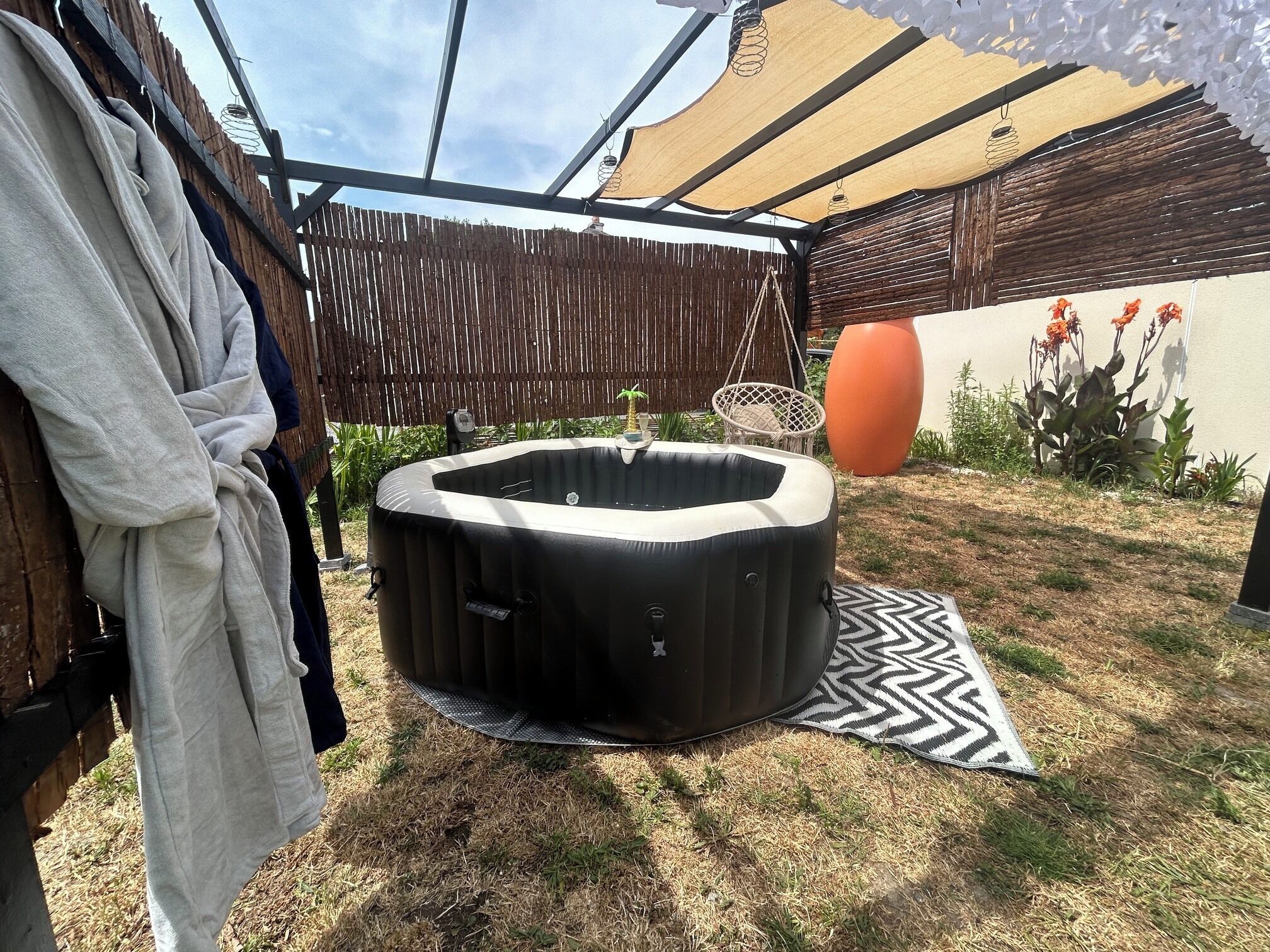 Un bain à remous dans un jardin, avec une clôture en bois, un hamac et une plante en pot.