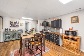Eine Küche mit Esstisch, Stühlen, einer Mikrowelle, Schränken und einer gefliesten Spritzschutzwand.